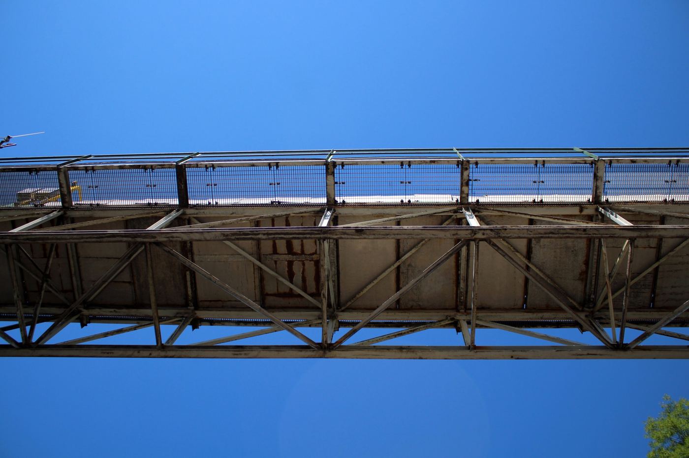 Underside view of the elevated conveyor bridge structure against a clear blue sky
