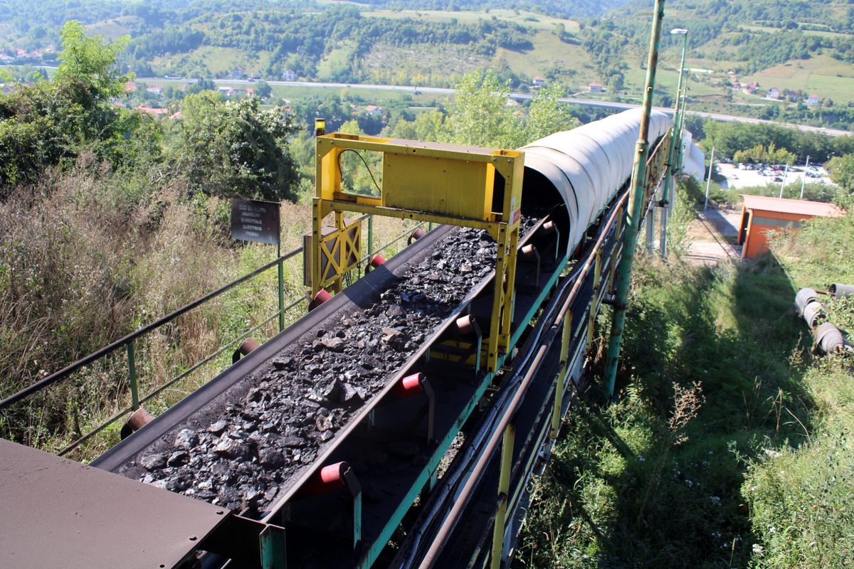 Conveyor carrying crushed coal past a safety light guard, with the Bosnia countryside in the background